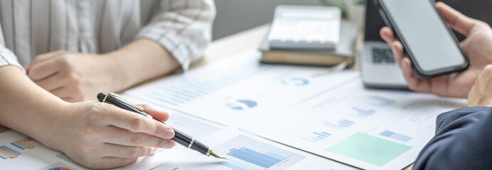 Business brainstorming, Female marketer analyzes graph data with executives and uses a mobile phone to monitor company performance in a conference room, Business team meeting.