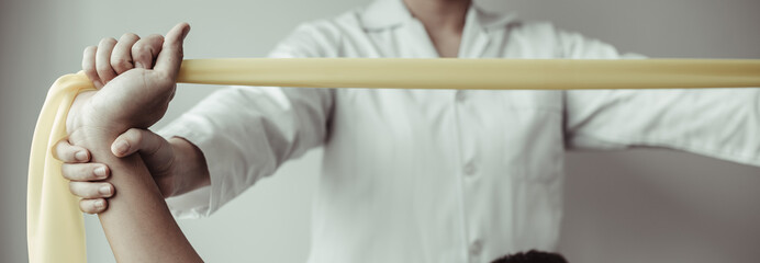 Physical therapy, Female physiotherapist uses an elastic band to test the arm injury of a male patient attending in clinic, Bone arrangement, Non-surgical medical treatment, Medical techniques.