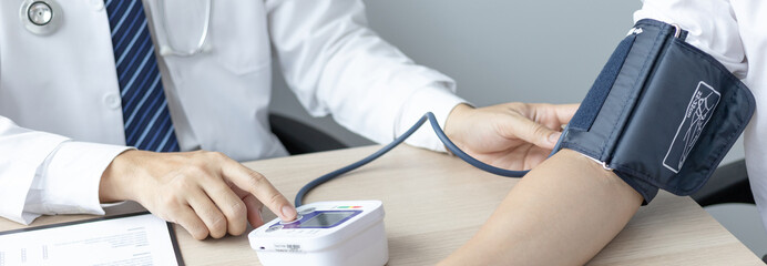 Male doctor uses a blood pressure monitor to check the body pressure and pulse of the patients who...
