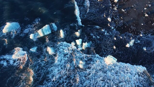 Pure blue Ocean water waves crush glacier ice at sunset, volcanic beach in Iceland