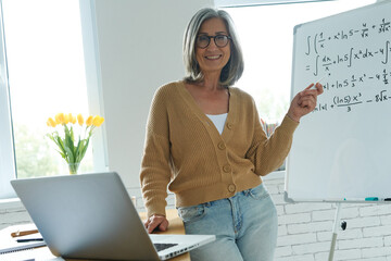 Cheerful senior woman pointing whiteboard while standing at the classroom