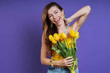 Attractive young woman holding a bunch of tulips and smiling while standing against purple background
