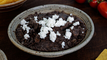 Mashed black beans meal with white fresh cheese. Black beans puree in bowl.