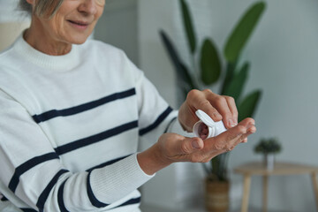 Close-up of senior woman taking medicines while sitting on the bed at home