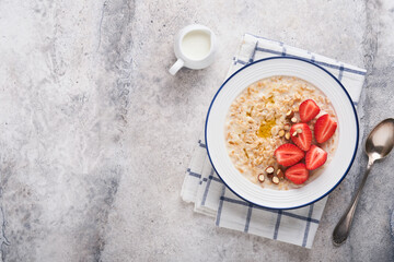 Oatmeal. Bowl of oatmeal porridge with strawberry, almond and milk on vintage light grey teal table. Top view in flat lay style. Natural ingredients. Hot and healthy breakfast and diet food.