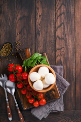 Caprese salad, ingredients for cooking. Cutting wooden board with traditional  caprese preparation ingridients: mozzarella, tomatoes , basil, olive oil, cheese, spices on wooden rustic background.