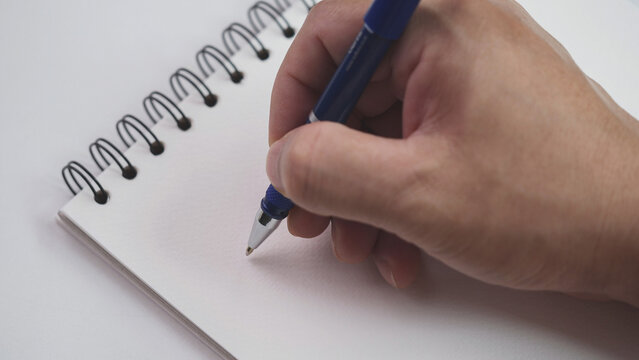 Close up hand writing paper on notebook with blue pen to note, memo, list action plan at office or home desk, selective focus. Concept of write on paper, letter, pen, notepad, diary