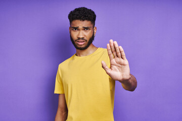 Young African man keeping his arm outstretched while standing against purple background