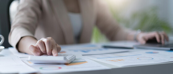Close up Business woman using calculator and laptop for do math finance on wooden desk in office and business working background, tax, accounting, statistics and analytic research concept