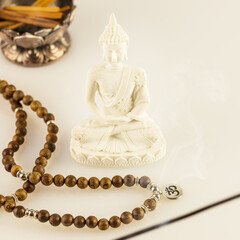 Buddha statue, prayer beads with symbol OM and aroma sticks on a white background. Asian spa ritual procedure, healing and meditation. Energetic health and relax. Vesak, Buddha Day. Soft image style