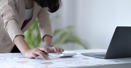 Close up Business woman using calculator and laptop for do math finance on wooden desk in office and business working background, tax, accounting, statistics and analytic research concept