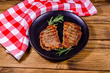 Plate with roasted steaks and rosemary twigs on a wooden table