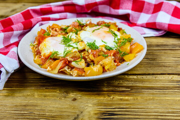 Homemade breakfast shakshuka with fried eggs, onion, bell pepper, tomatoes and dill on a wooden table. Jewish cuisine