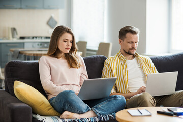 Couple of young woman and middle aged man sitting together on sofa at home and working remotely on laptop computers