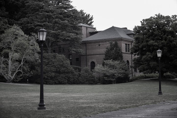 Fototapeta premium Two Unlit street lamp lanterns with a grass field and a building in the background in Black and White