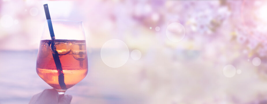 Cheers with a glass of cocktail on a sunny terrace with garden view. Horizontal background for wedding and romantic concepts. 