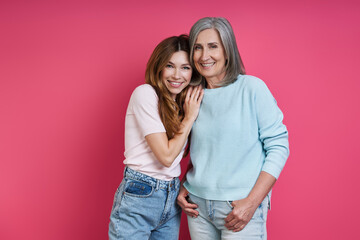 Happy mother and adult daughter bonding against pink background