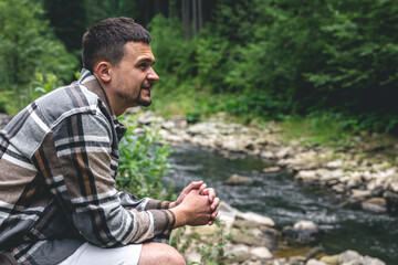 A young man in the forest near the river enjoys nature, a halt.