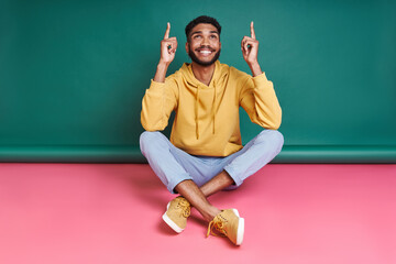 Cheerful African man pointing up while sitting against colorful background