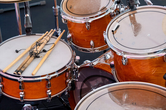 Close up brown wooden drum kit, consisting of cymbals, floor tom-tom, bass and snare drum, hi-hat, not new with battered drumsticks,no people, before concert. Musical instruments and learning concept.