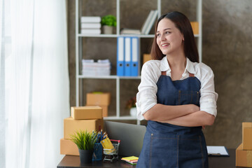 Smiling young Asian business owner woman prepare parcel box and check online orders of product for deliver to customer on laptop computer. Online merchandising concept.