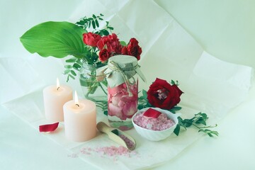 Bouquet of fresh red roses, water with pink rose petals, sea salt and burning candles, on a light background, natural cosmetics, body care, emotion of love