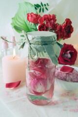 Obraz na płótnie Canvas Bouquet of fresh red roses, water with pink rose petals, sea salt and burning candles, on a light background, natural cosmetics, body care, emotion of love