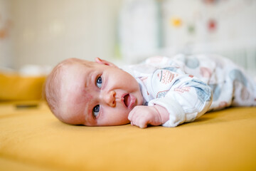 A newborn cute baby is lying on his stomach on a yellow sofa