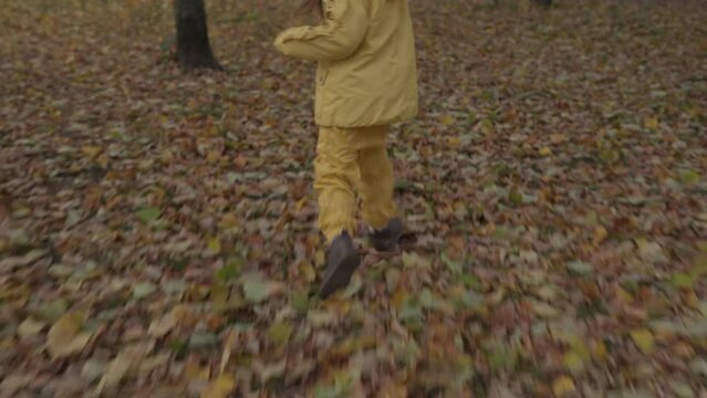 One happy funny active smilling friends child kid walking running legs shoes in park forest enjoying autumn falling leaves nature weather. Kid in yellow cloth playing hiding behind trees Slow motion