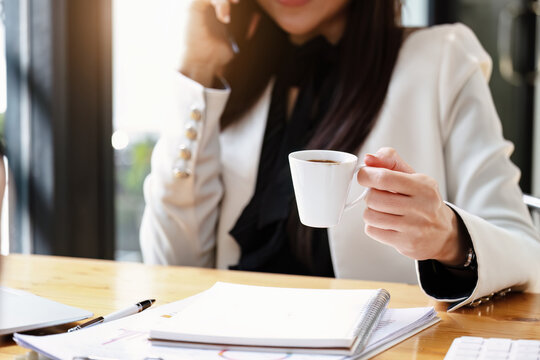 young Asian businesswoman drinking coffee and talking on the phone while working