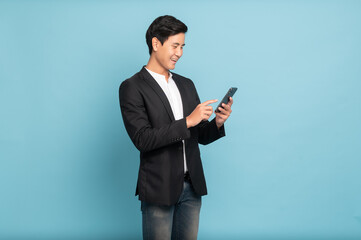 Young asian man in suit and jeans using smartphone exciteing with news on phone for smart casual business concept isolated on blue background