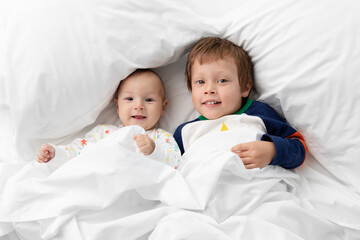 Newborn baby and big brother lying together on white bed