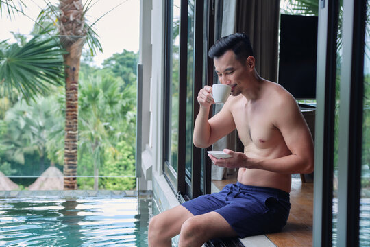 Happy man in swimsuit drinking coffee by luxury pool in hotel or tropical resort. Relaxing, Exotic summer travel, holiday, vacation and weekend