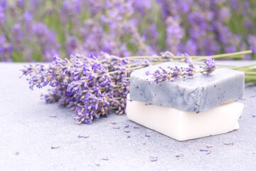 Natural handmade soap bars against lavender flowers field as background with copy space. Craft herbal cosmetics, lavender beauty products - obrazy, fototapety, plakaty