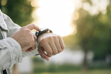 Close up shot of male's hand uses of wearable smart watch at outdoor in sunset. Smart watch. Smart watch on a man's hand outdoor. Man's hand touching a smartwatch