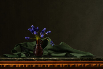 Bouquet of blue hercinthus muscari flowers on a green marble table. Green scarf. Dark background. Reflection. Thoughtfulness, calmness, peace, silence. Beautiful still life. Peace inside.