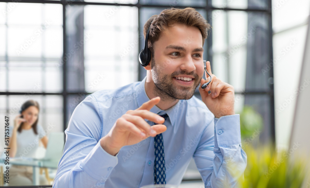 Sticker Cheerful young support phone male operator in headset, at workplace while using computer, help service and client consulting call center concept.