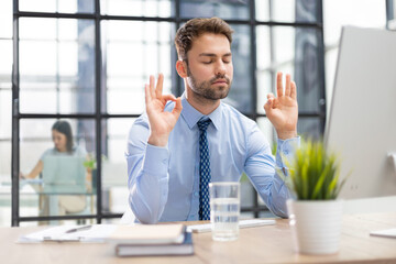 Calm handsome businessman meditate keeping mudra listening to relaxing music at office desk,...
