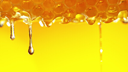 Honey dripping from honey comb on golden background.