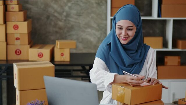 Female Muslim monger is packing products for online selling in to cardboard boxes for delivery shipping.