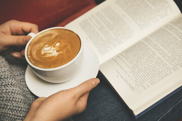 Woman with cup of coffee reading book, closeup