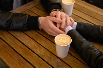 Lovely couple with coffee holding hands together at wooden table outdoors, closeup. Romantic date