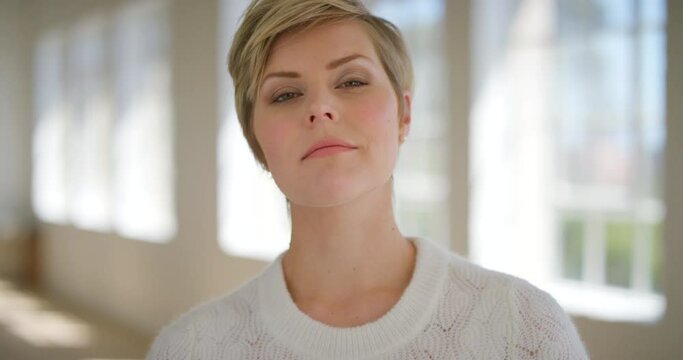Face of an edgy blonde woman with attitude inside a room. Slow motion portrait of a confident or arrogant young girl looking proud. A creative female with a daring expression in her office