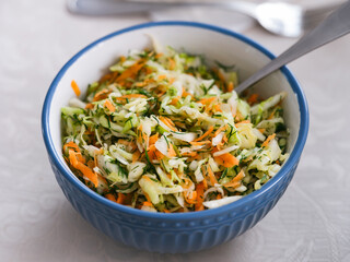Vegan salad with chopped cabbage, carrot and dill in a blue bowl with a fork.