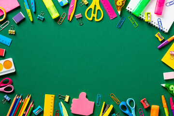 Back to school concept. Frame made of colorful school or office supplies on green table. Flat lay, top view, copy space.
