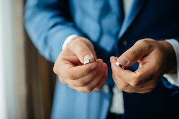 wedding rings in the hands of the groom, the groom in a blue suit
