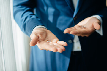 wedding rings in the hands of the groom, the groom in a blue suit