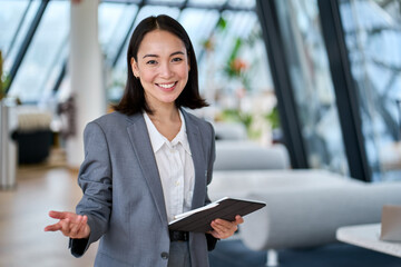 Happy young Asian saleswoman looking at camera welcoming client. Smiling woman executive manager, secretary offering professional business services holding digital tablet standing in office. Portrait - Powered by Adobe