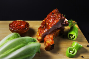 Fried and smoked pork ribs covered with "Ajika" sauce with fresh vegetables on a cutting board. Shallow depth of field
