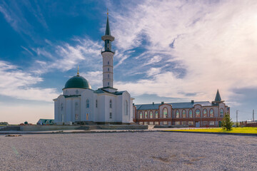 Muslim mosque with minaret and madrasah against blue cloudy summer sky.